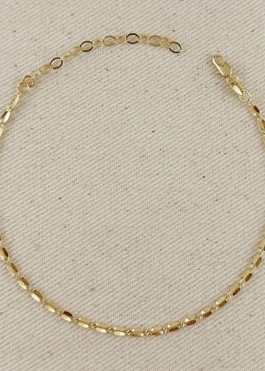 Gold chain bracelet on a beige fabric background