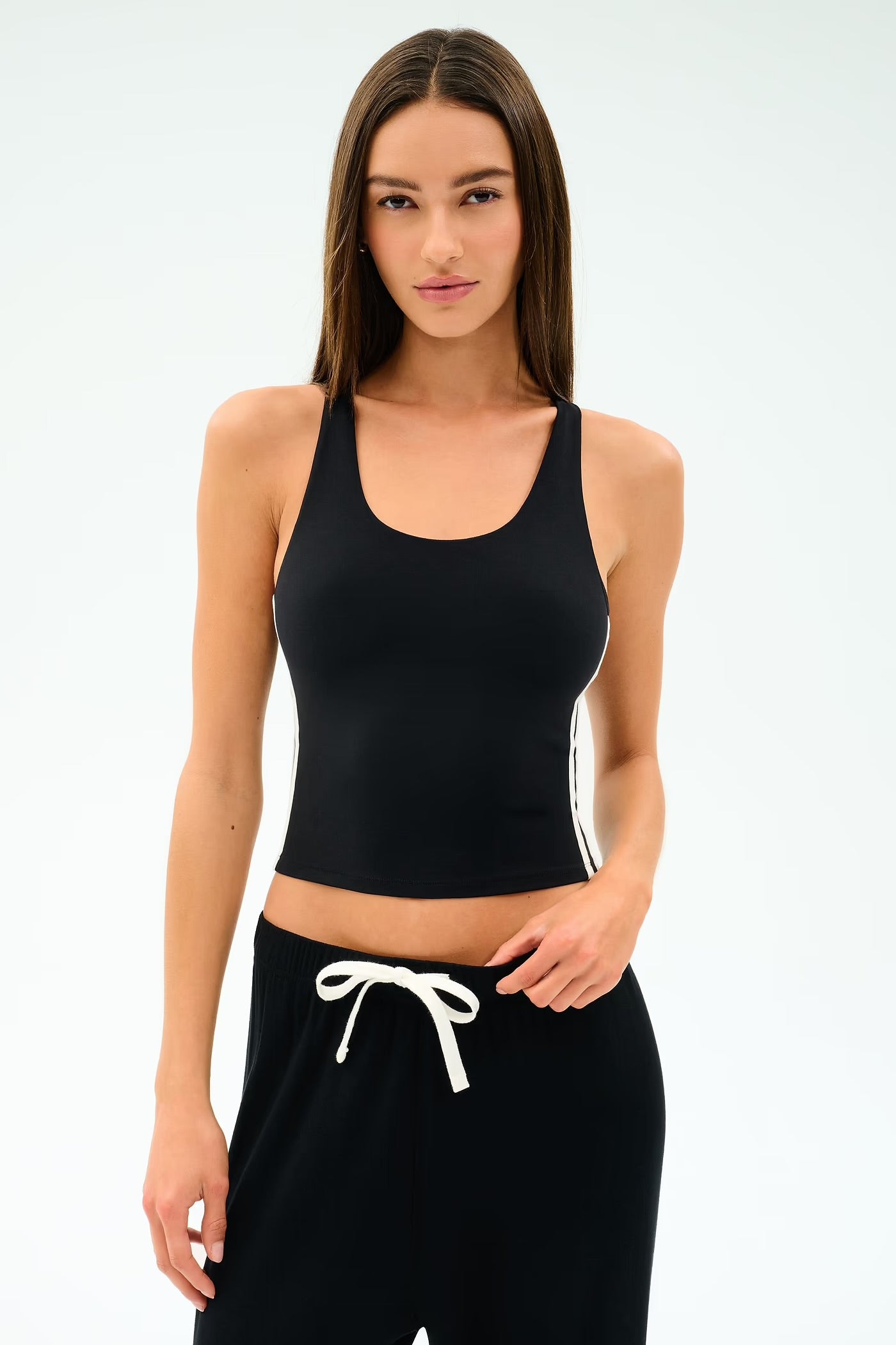 Woman wearing a black tank top and black pants with white drawstrings