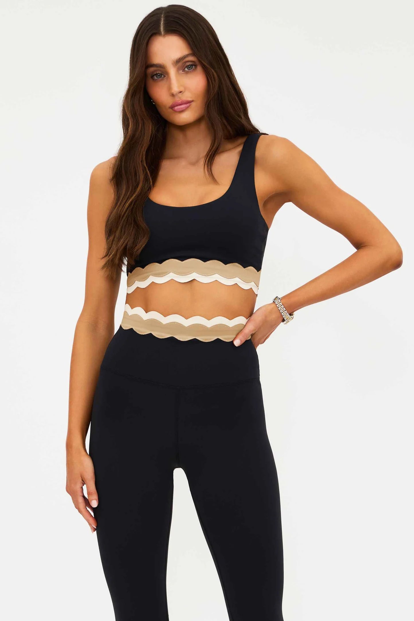 Woman wearing a black tank top with a beige ruffled detail and black leggings 