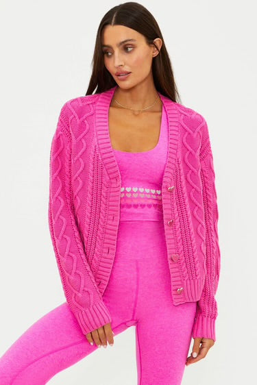 Woman wearing a pink cable knit cardigan over a matching outfit.