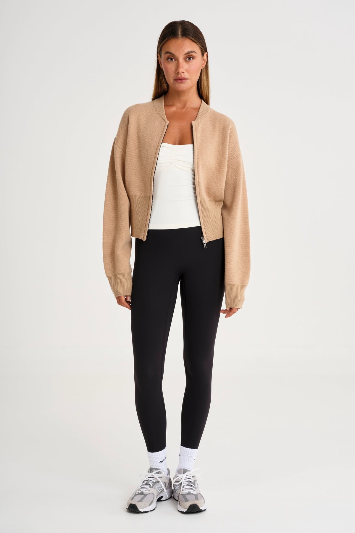 Woman wearing a beige blazer, white top, black leggings, and sneakers 