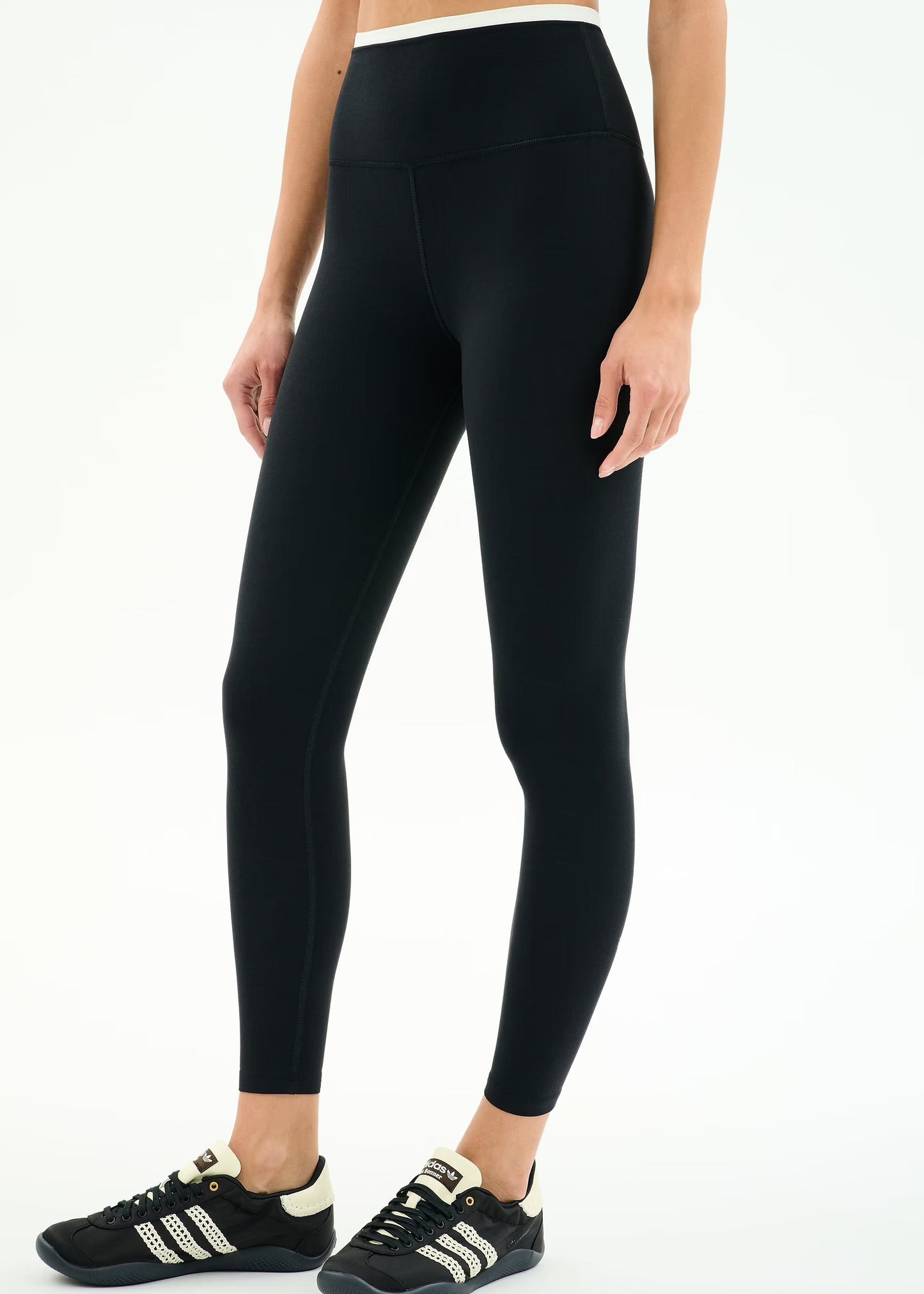 Person wearing black leggings and black sneakers with white stripes on a white background