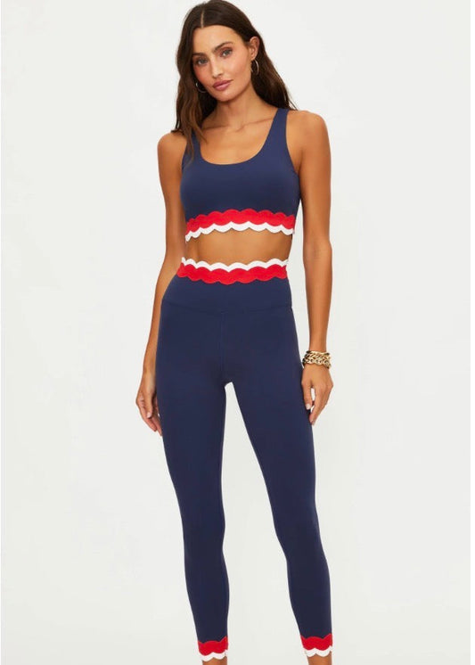 Woman wearing a navy sports bra and leggings with red accents on a white background