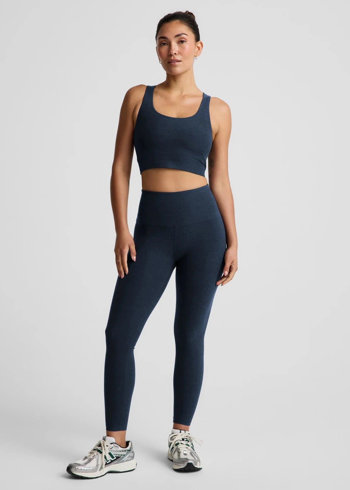 Woman wearing a navy blue sports bra and leggings set on a light gray background