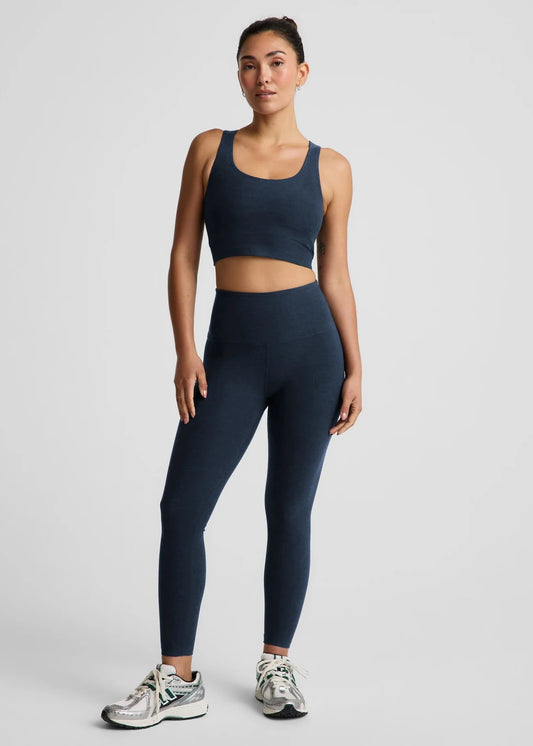 Woman wearing a navy blue sports bra and leggings set on a light gray background