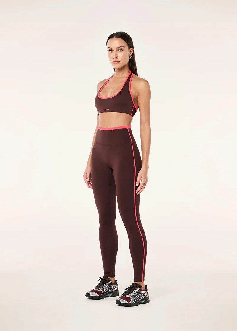 Woman wearing a brown sports bra and leggings with pink accents on a white background