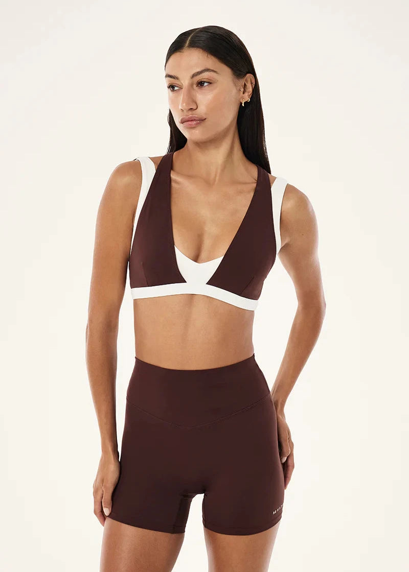 Woman wearing a brown and white sports bra and shorts on a beige background