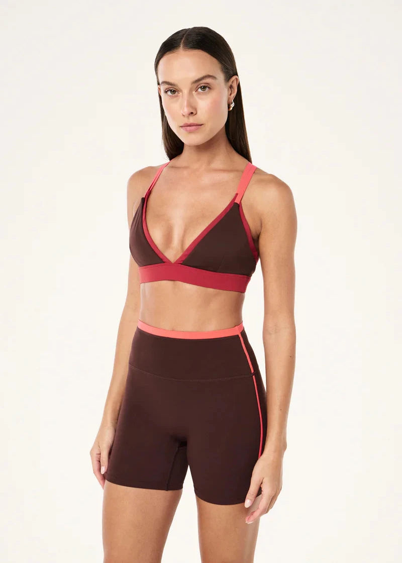Woman wearing a brown and pink sports bra and shorts set on a white background